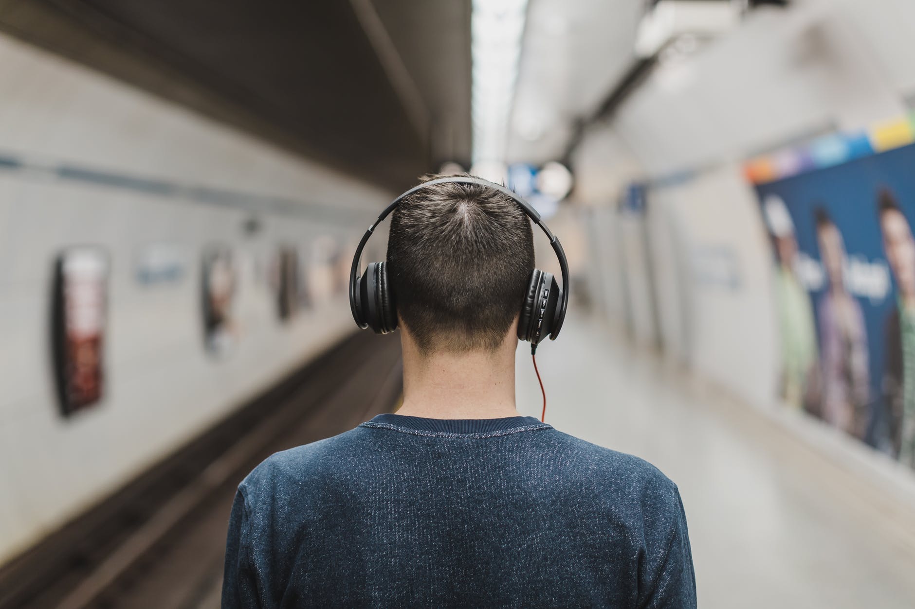 man wearing black headphones beside train rail